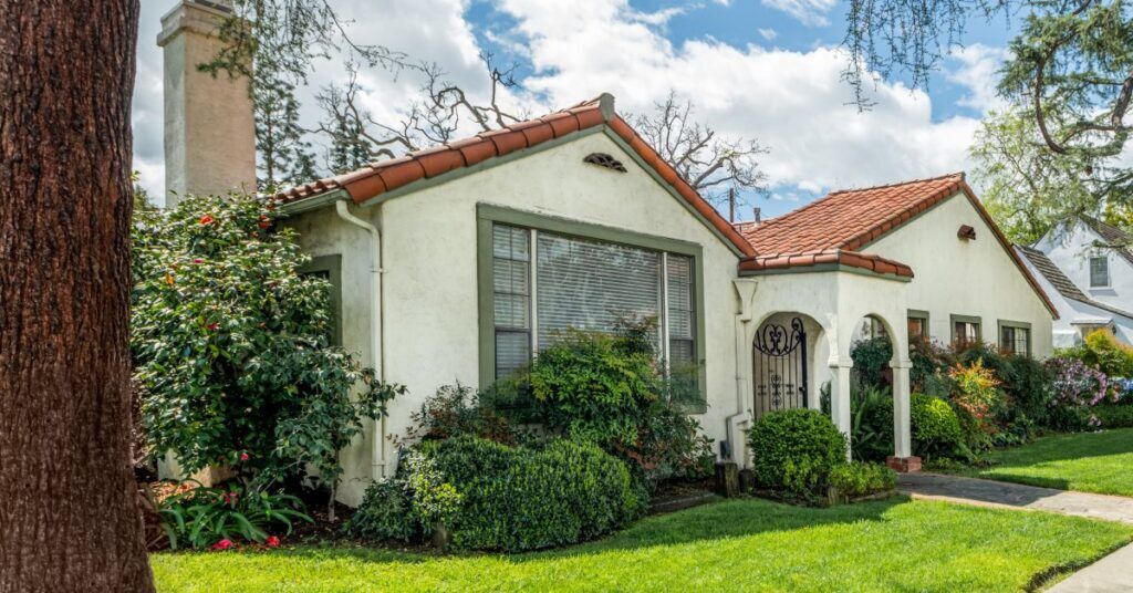 A nice suburban home with a vibrant green yard, stucco walls, a clay tile roof, and a chimney.