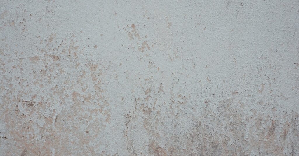A close-up of an old wall where white paint has begun to fade and reveal the reddish-brown layer beneath.