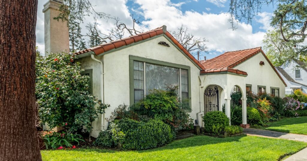 A nice suburban home with a vibrant green yard, stucco walls, a clay tile roof, and a chimney.
