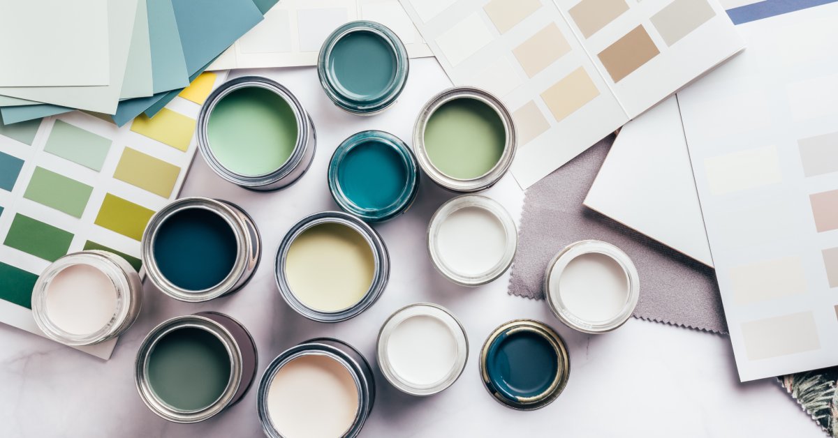 Numerous paint samples and small, open cans of paint in various colors are spread out on a white table.